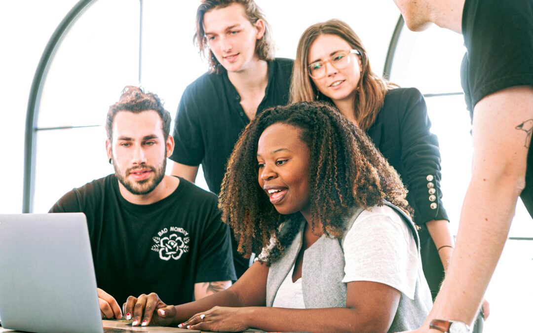 A diverse group of young professionals collaborating around a laptop in a modern office setting. Perfect for business or tech concepts.