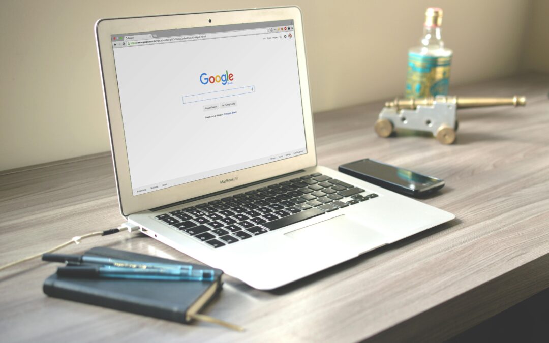 A neat workspace featuring a laptop displaying Google search, a smartphone, and a notebook on a wooden desk.